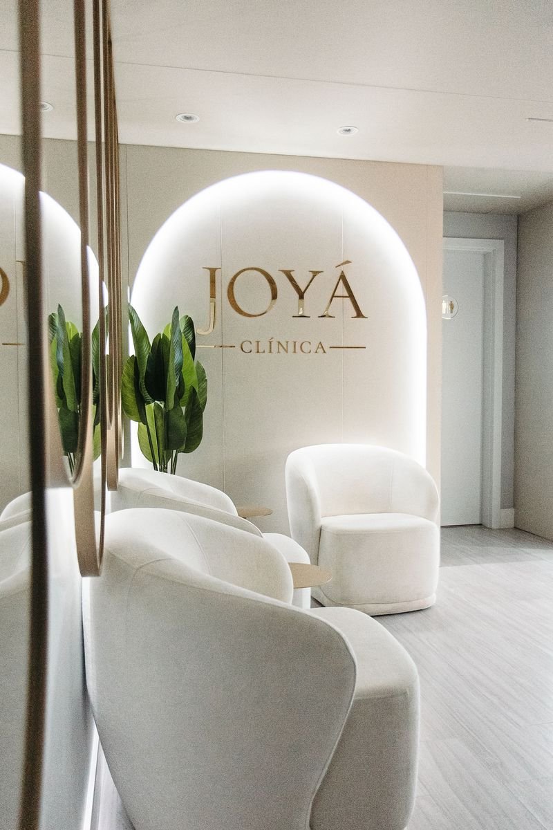 Recepção da Clínica Joyá, com arco iluminado, logotipo dourado e poltronas brancas